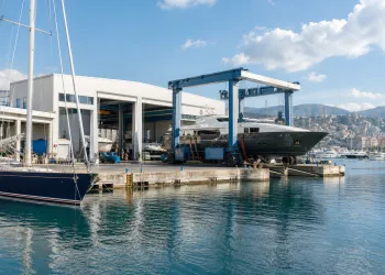 Travel-lift che solleva uno yacht accanto a capannoni e banchine di un cantiere navale sul porto