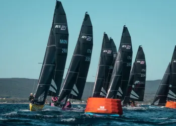 Barche della classe RS21 in regata attorno a una boa arancione con vele nere e numeri identificativi.