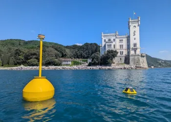 Boe gialle strumentate in mare davanti a una costa con un edificio storico, per rilevazioni in situ