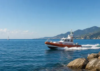 Gommone della Guardia Costiera in navigazione lungo la costa, con scafo arancione e mare calmo