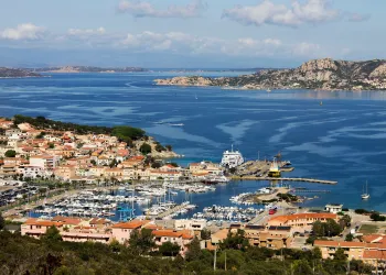 Panoramica di un porto turistico con marina, traghetti e case lungo una costa rocciosa.