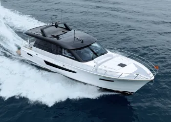 Yacht a motore bianco con tetto scuro e senza flybridge in navigazione veloce, con scia bianca sul mare scuro, visto dall'alto