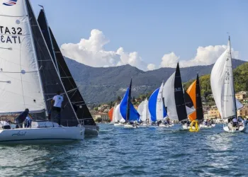 Barche a vela della flotta Protagonist 7.50 in regata davanti a Salò con colline e paese sullo sfondo
