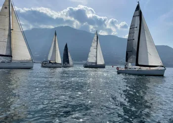 Vele e imbarcazioni a vela che navigano su acque calme con montagne sullo sfondo