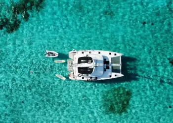 Veduta aerea di un catamarano bianco ancorato in acque turchesi con gommoni e tavole accanto