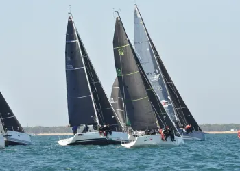 Barche a vela da regata con vele scure e equipaggi appesi al bordo, in prossimità di una boa