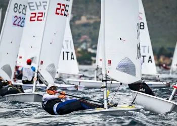 Velisti in regata su dinghy monotipo con vele numerate, in primo piano un timoniere sbilanciato fuori bordo sul mare mosso
