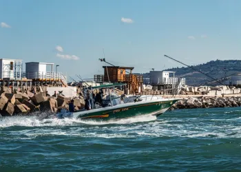 Barca da pesca a motore che naviga vicino al molo con canne da pesca in evidenza