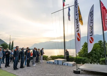 Partecipanti in piedi durante l'alzabandiera sul lungolago con bandiere e podio
