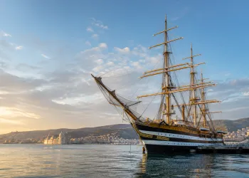 Nave scuola a vela ormeggiata al porto al tramonto con lo skyline della città sullo sfondo
