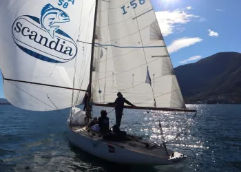 Barca a vela d'epoca con spinnaker Scandia e numero velico I-58, equipaggio a bordo, su un lago con montagne sullo sfondo