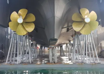 Due eliche in bronzo sotto lo scafo di una nave sorretto da cavalletti in bacino di carenaggio