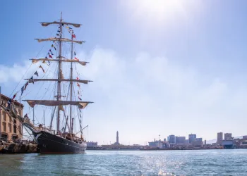 Brigantino a tre alberi attraccato al Porto Antico di Genova con skyline cittadino e sole