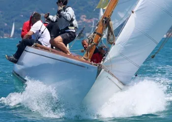 Imbarcazione a vela storica inclinata con equipaggio mentre taglia le onde durante una regata