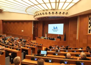 Sala parlamentare con partecipanti seduti ai banchi e un relatore al podio, sotto uno schermo con il logo BlueMarina Awards