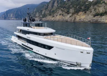 Superyacht bianco a motore in navigazione davanti a una costa rocciosa