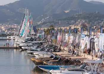 Banchina affollata di barche e stand con bandiere al porto durante un salone nautico