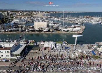 Flotta di derive e vele allineate sul lungomare davanti al porto di Rimini, pronte per la regata