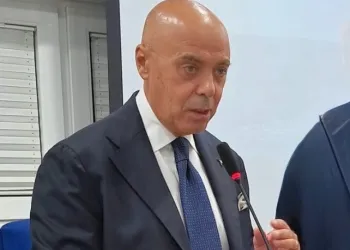 Uomo in giacca e cravatta che parla al microfono durante un intervento in sala.