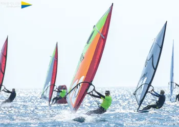 Windsurfer con vele colorate che scivolano sul mare scintillante