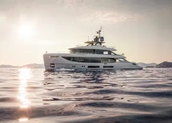 Yacht di lusso bianco in navigazione su mare calmo al tramonto, con il sole basso e colline sullo sfondo