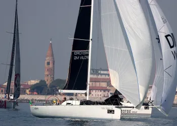 Barche a vela da regata con grandi spinnaker issati davanti a edifici costieri