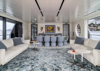 Salone interno luminoso di uno yacht con divani bianchi, grande tavolo da pranzo e tappeto blu