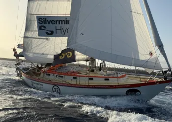 Barca a vela con scafo bianco e filo rosso, numero 22 e scritta Silvermines Hydro sulle vele, naviga con onde e schiuma in primo piano.