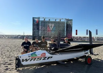 Barca WASZP sulla spiaggia con un gruppo di persone e un palco del Race Village sullo sfondo