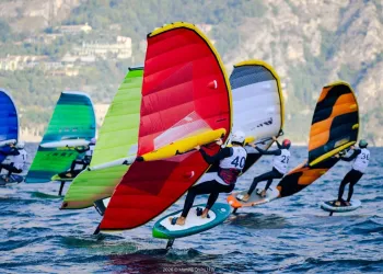 Gruppo di wingfoiler con ali colorate rosse, verdi, blu e arancioni che navigano sul lago con numeri di vela sulle casacche