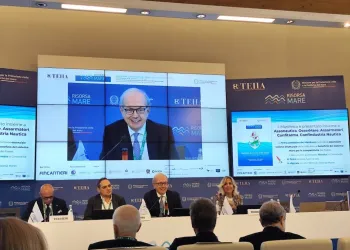 Tavola rotonda con relatori seduti a un tavolo e un grande schermo che mostra uno speaker durante un convegno sulla nautica.