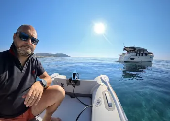 Uomo seduto su un gommone vicino a una barca a motore in mare calmo sotto un cielo sereno