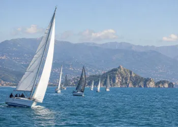 Vele e imbarcazioni da regata in acqua con l'Isola Palmaria e la costa sullo sfondo.