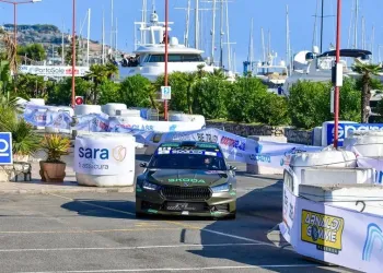 Auto da rally che percorre il tracciato tra barriere nel porto con yacht e barche sullo sfondo
