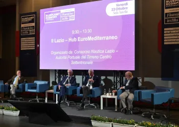 Quattro relatori seduti su poltrone blu sul palco di un convegno, davanti a un grande schermo con il titolo 