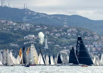 Molte barche a vela in regata davanti a una costa collinare