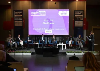 Relatori seduti sul palco davanti a uno schermo con la scritta Blue Finance, mentre una donna parla al microfono; in primo piano il pubblico.