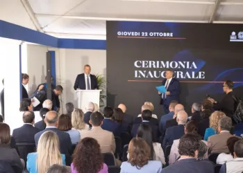 Cerimonia inaugurale con un relatore al podio davanti al pubblico seduto, sotto un tendone con schermo che riporta la data 22 ottobre