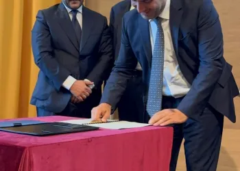 Due uomini in giacca e cravatta che firmano documenti su un tavolo con tovaglia rossa