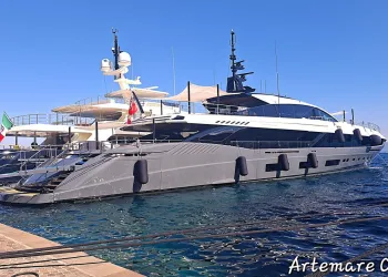 Superyacht open grigio con ampie vetrate scure ormeggiato in banchina, con parabordi neri e mare blu sotto un cielo sereno