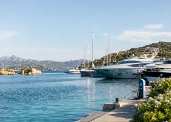 Banchina con yacht e imbarcazioni ormeggiate davanti a costa rocciosa e colline