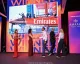 Premiazione su palco con schermo che mostra un catamarano Emirates e persone che si stringono la mano