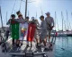 Equipaggio giovane sul ponte di una barca da regata che tiene una bandiera nel porto di Trieste.