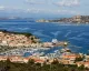 Panoramica di un porto turistico con marina, traghetti e case lungo una costa rocciosa.