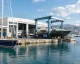 Travel-lift che solleva uno yacht accanto a capannoni e banchine di un cantiere navale sul porto