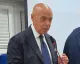 Uomo in giacca e cravatta che parla al microfono durante un intervento in sala.