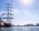 Brigantino a tre alberi attraccato al Porto Antico di Genova con skyline cittadino e sole