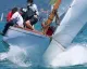 Imbarcazione a vela storica inclinata con equipaggio mentre taglia le onde durante una regata